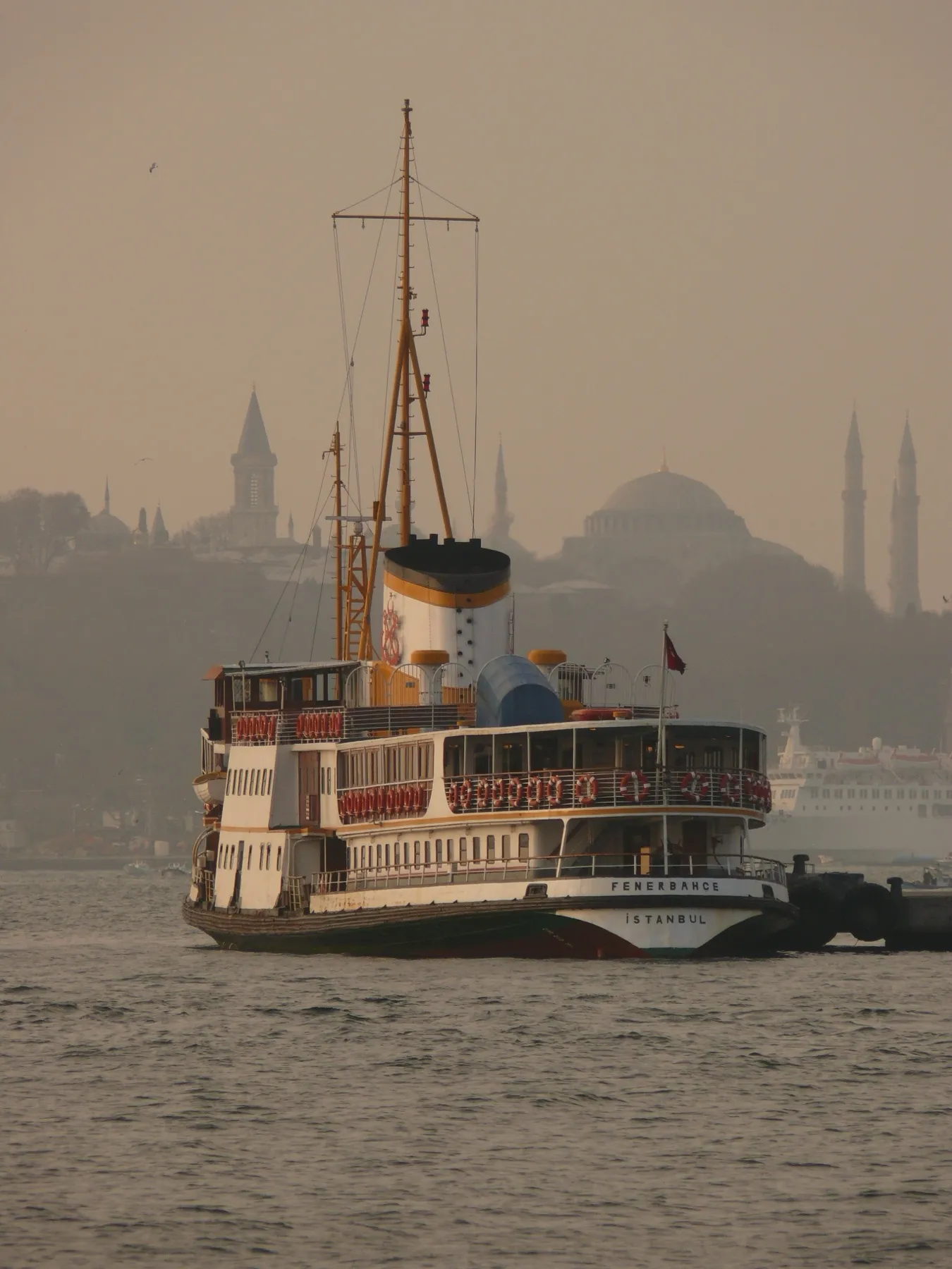 A ferry in the haze with the domes and minarets of the old city behind
